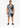 A man stands wearing a short-sleeve shirt and matching shorts with a black and white palm leaf pattern.