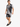 A man wearing a black and white palm leaf patterned short-sleeve shirt and matching shorts, paired with black sneakers.