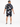 A man stands with his back to the camera, wearing a colorful button shirt and matching shorts with abstract patterns.