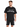 A man stands wearing a black oversized t-shirt with graphic text and matching black shorts featuring a large number.