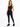 A model poses in a sleek black one-shoulder activewear top paired with matching leggings and sneakers.