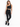 A model poses in a sleek black one-shoulder activewear top paired with matching leggings and black sneakers.