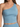 A woman is wearing a light blue, one-shoulder crop top with a fitted design and smooth fabric.