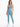 A woman stands confidently in a light blue one-shoulder crop top and matching leggings, paired with white sneakers.