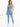 A model poses in a light blue one-shoulder crop top paired with matching high-waisted leggings and white sneakers.
