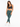 A model poses in fitted green leggings paired with a dark sports bra and white sneakers against a plain background.