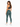 A woman stands with her back to the camera, wearing green leggings and a dark sports bra, paired with white sneakers.