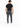 A man stands with his back to the camera, wearing a black t-shirt and gray tapered pants with zippers.