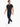 A man walks confidently in a fitted black t-shirt and navy pants, paired with white sneakers and a chain detail.