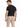 A man stands with his back to the camera, wearing a black t-shirt and beige evening pants with a chain detail.