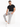 A man sits on a white pedestal wearing gray evening pants and a black t-shirt, paired with white sneakers.