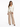A woman stands confidently in a fitted cream jacket paired with beige wide-leg trousers and black heels.