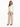 A woman stands confidently in a fitted cream jacket paired with beige trousers and stylish black heels.