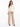 A woman stands confidently in a fitted cream jacket paired with beige wide-leg trousers and black heels.