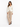 A woman in a fitted cream jacket paired with beige trousers and black heeled sandals, standing against a white backgr...