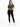 A woman stands wearing a cropped olive green top tied at the waist, paired with black leggings and white sneakers.