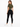 A woman in a cropped olive green top and black leggings poses from the back, showcasing a casual outfit.