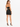A woman stands with her back to the camera, wearing a fitted black skirt and matching crop top, paired with black heels.