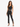 A model poses in a fitted black crop top and matching high-waisted pants with side slits, paired with strappy heels.