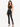 A model poses in a fitted black crop top and high-waisted pants with side slits, paired with strappy heels.