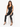 A woman sits on a white pedestal wearing a black ribbed crop top and fitted pants with side slits.