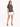 A woman stands confidently in a gray t-shirt paired with a white mini skirt and black high-heeled sandals.