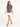 A woman walks confidently in a gray tee with a stylish graphic, paired with a white skirt and black heels.