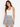 A woman poses in a fitted white tank top and a pleated black and white patterned skirt against a plain background.