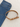 A tan leather belt with a gold buckle positioned next to folded blue denim jeans on a light fabric background.