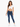 A woman stands confidently in a cropped white top and fitted blue jeans, paired with white sneakers.