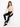 A model sits on a white cube, wearing a fitted beige long-sleeve top with cutouts and black skinny jeans.