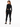 A woman in a black ribbed bodysuit with an open back, paired with black skinny jeans and sneakers.