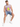 A man sits on a white pedestal wearing a sleeveless graphic shirt and denim shorts, paired with white sneakers.