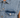 Close-up of a light blue denim vest featuring a pointed collar and a chest pocket with a silver snap button.