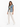A woman stands confidently in a sleeveless denim vest, paired with a light green top and cream-colored pants.