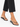 Ankle adorned with a colorful beaded chain, paired with black flip-flops and cropped black pants.