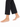 A bare foot adorned with a delicate gold anklet featuring colorful charms, paired with black cropped pants.