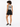 A woman with curly hair wears a patterned bodysuit and high-waisted black shorts, standing with her back to the camera.