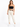 A woman stands confidently in a black cropped top, cream-colored pants, and white sneakers, showcasing a stylish outfit.