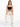 A model poses on a stool wearing a black cropped top, beige pants, and white sneakers, showcasing a casual look.