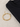 Gold bracelet with geometric links and a lobster clasp, placed beside a folded black garment on a textured surface.