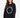 A woman with long, wavy hair wears a black oversized sweatshirt featuring a circular text design in white.