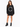 A woman stands wearing a black oversized sweatshirt with a circular white text design, paired with black chunky boots.