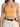 A close-up of a woman wearing a fitted orange crop top with thin straps, paired with high-waisted beige trousers and...