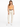 A woman stands wearing a fitted orange top, beige high-waisted pants, and white sneakers, with a braided belt.