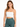 A model wearing a fitted white crop top with thin straps paired with high-waisted green leggings.