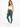 A model poses in a fitted white crop top and teal leggings, paired with white sneakers against a plain background.