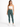 A woman stands confidently in a fitted white crop top and high-waisted green leggings, paired with white sneakers.