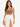 A woman poses in a fitted brown top and a flowing white skirt with high side slits, showcasing a stylish look.