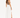 A woman stands in profile wearing a fitted brown top and a flowing white skirt with a side slit.